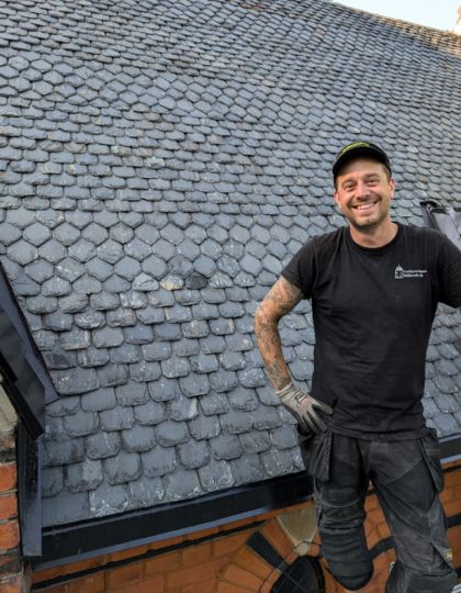en man i svarta arbetskläder står vid ett skiffertak han arbetar med